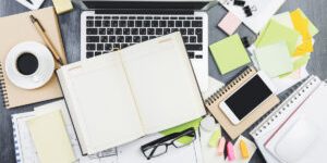 Mix of office supplies, laptop computer and mobile phone on contemporary wooden table top with other items. Above view. Mock up